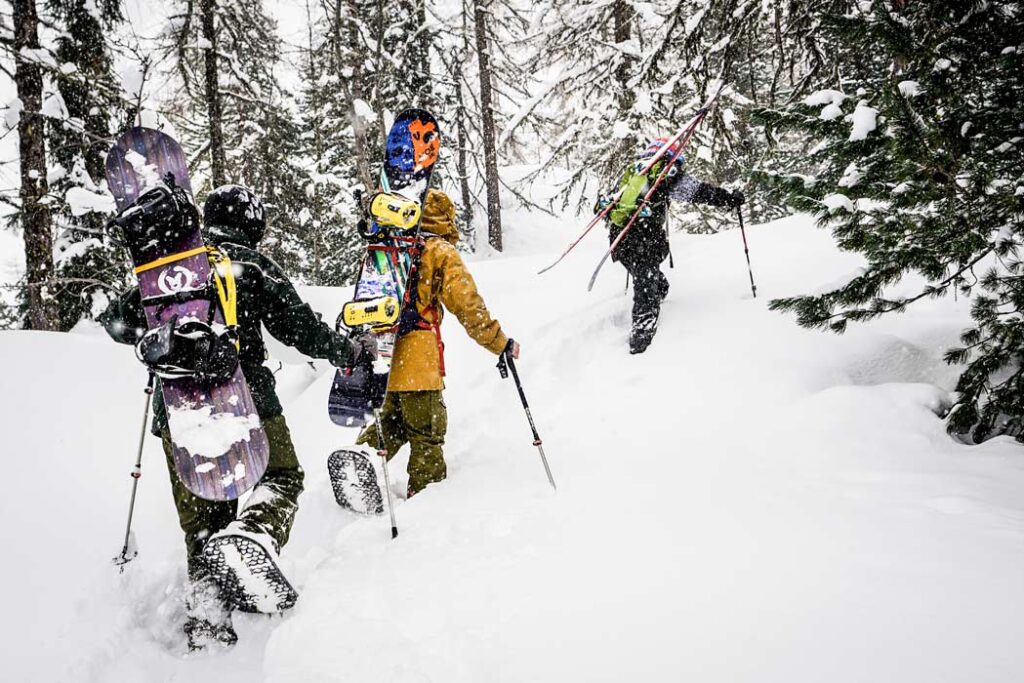 3 snowboarders hiking up a snowy backcountry slope while wearing Snowfoot Snowshoes