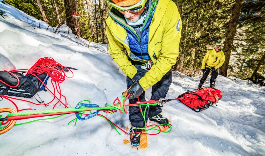 Two snow rescue team members wearing Snowfoot snowshoes while pulling a body sled through a snowy mountain forest