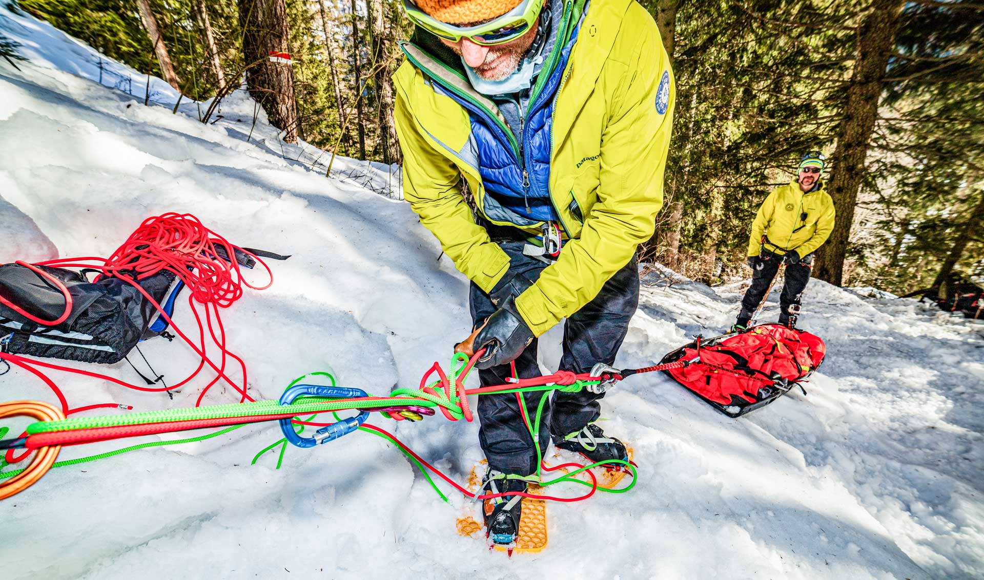 Two snow rescue team members wearing Snowfoot snowshoes while pulling a body sled through a snowy mountain forest
