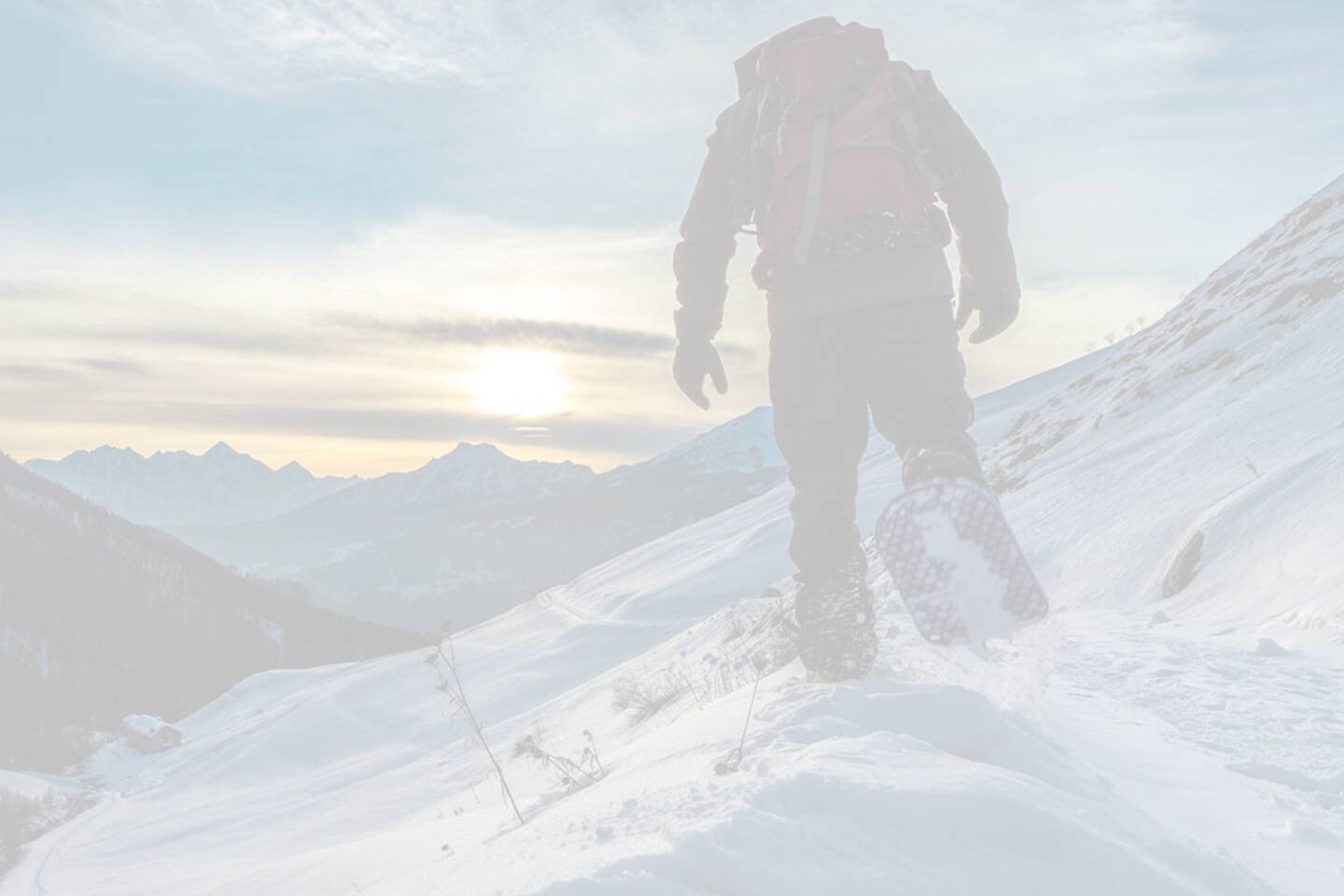 A snowshoer walking toward the sunrise on the side of a mountain