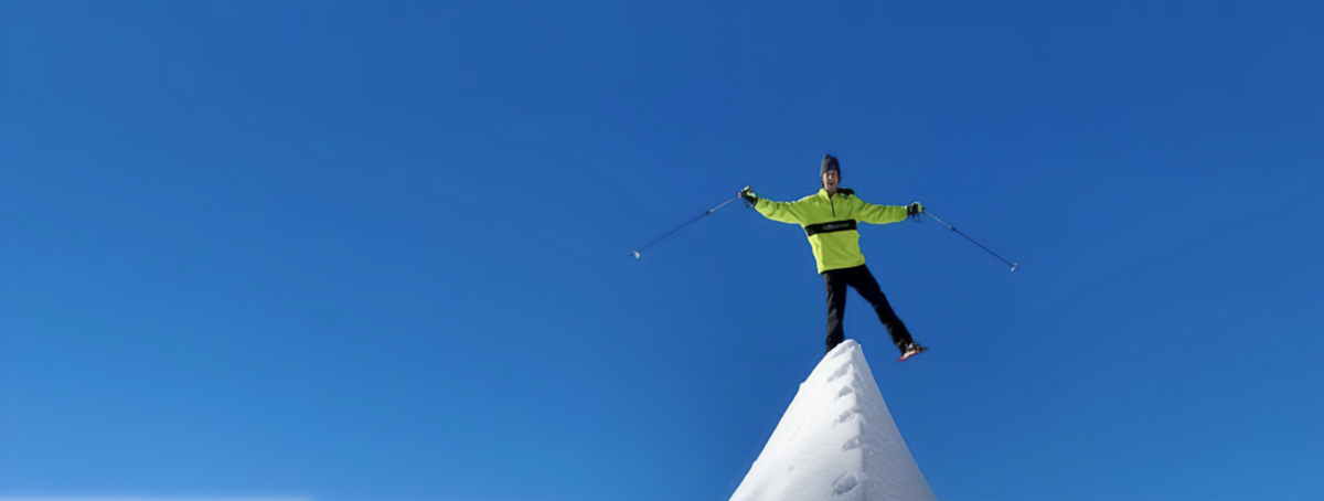 A person wearing Snowfoot Snowshoes while balancing on one foot on the ridge of a mountain