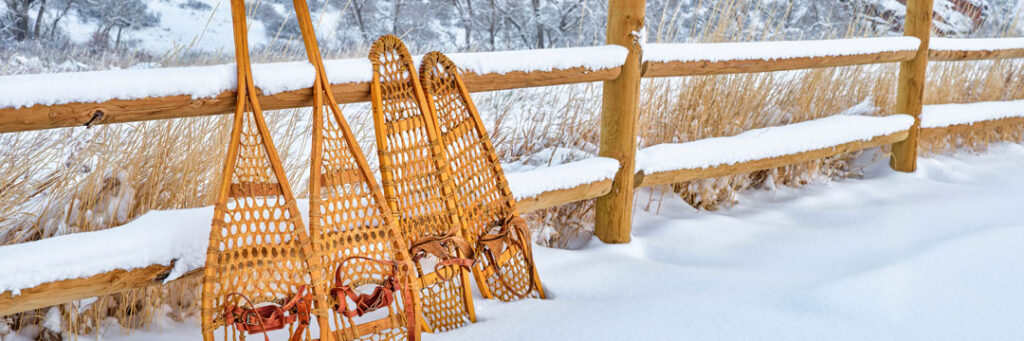 two sets of antique wooden snowshoes leaning against a snow covered fence with a mountain in the background