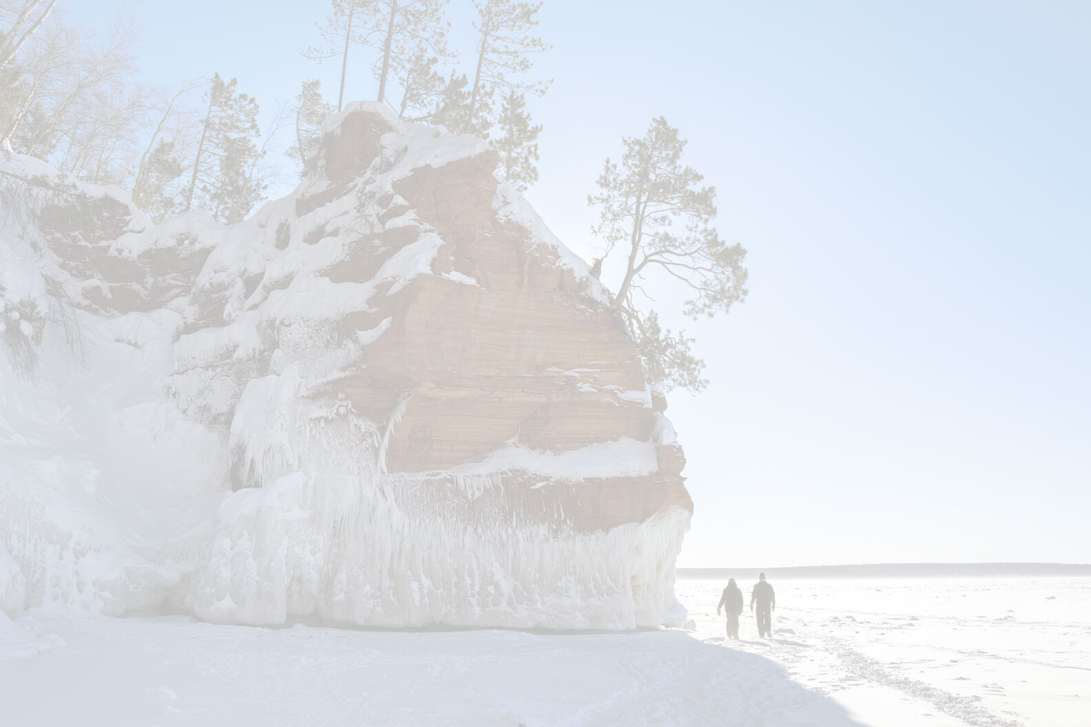 Lake Superior frozen in winter as two people snowshoe through the landscape