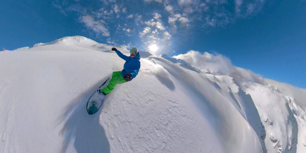 A snowboarder riding down the peak of a mountain off piste