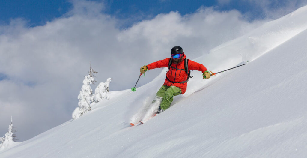 dynamic photo of a skier in a red jacket carving lines on a backcountry mountain slope