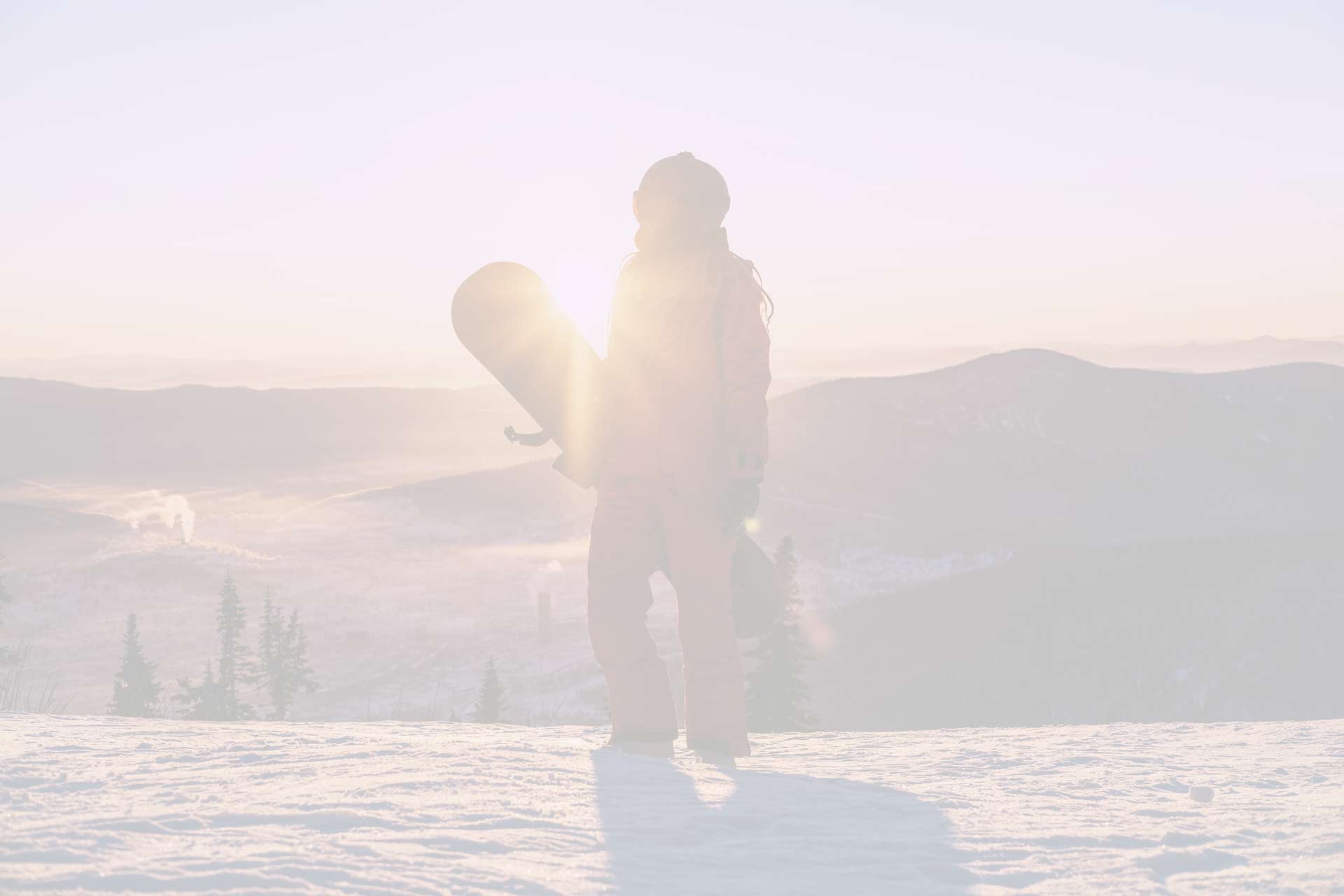 A snowboarder after climbing a remote mountain carrying his snowboard ready for a backcountry adventure