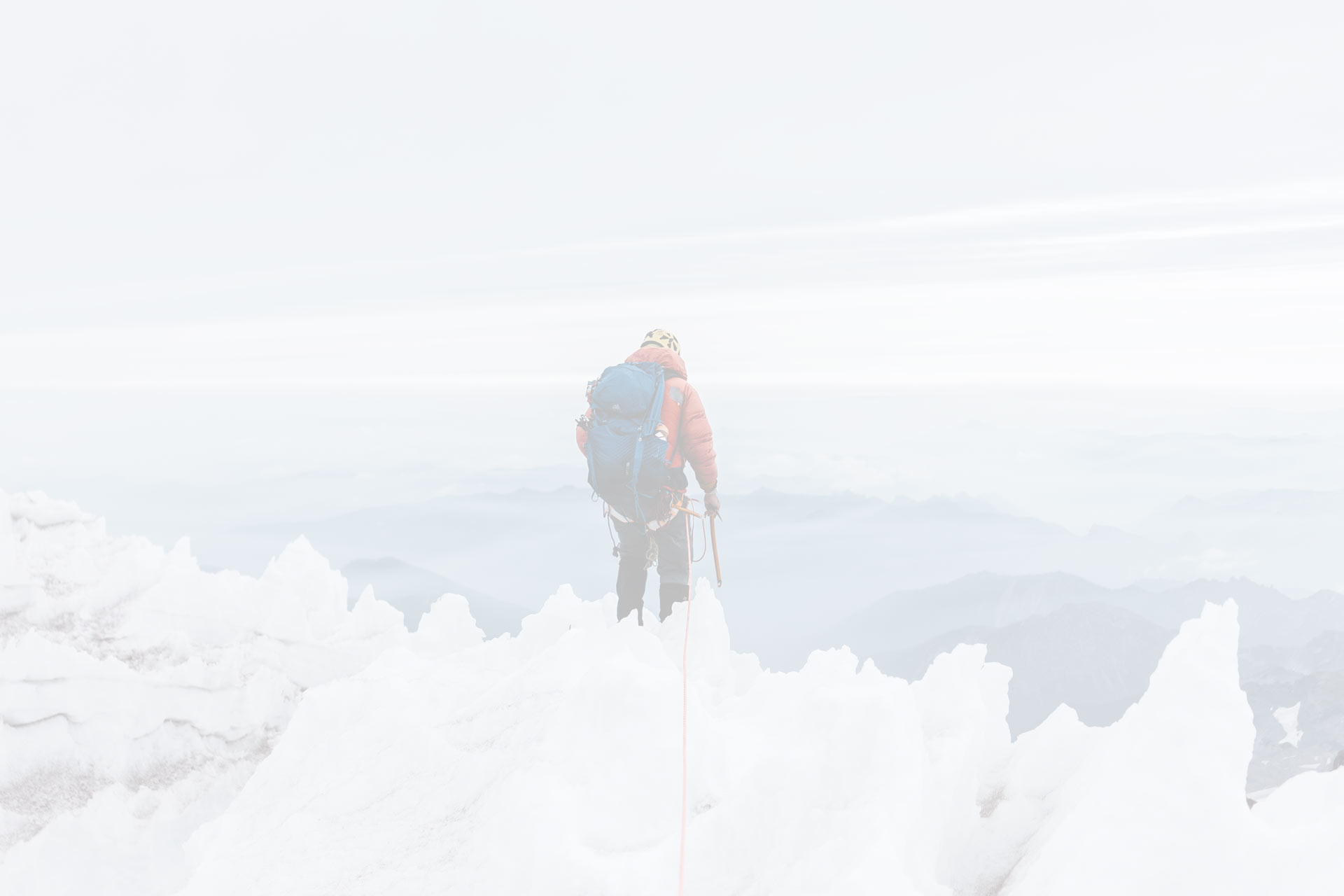man standing on a snowy peak looking over a landscape of mountains in Mount Rainer National Park