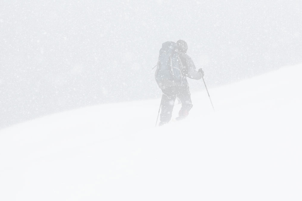 A snowshoer hiking up a snowy mountain in a blizzard