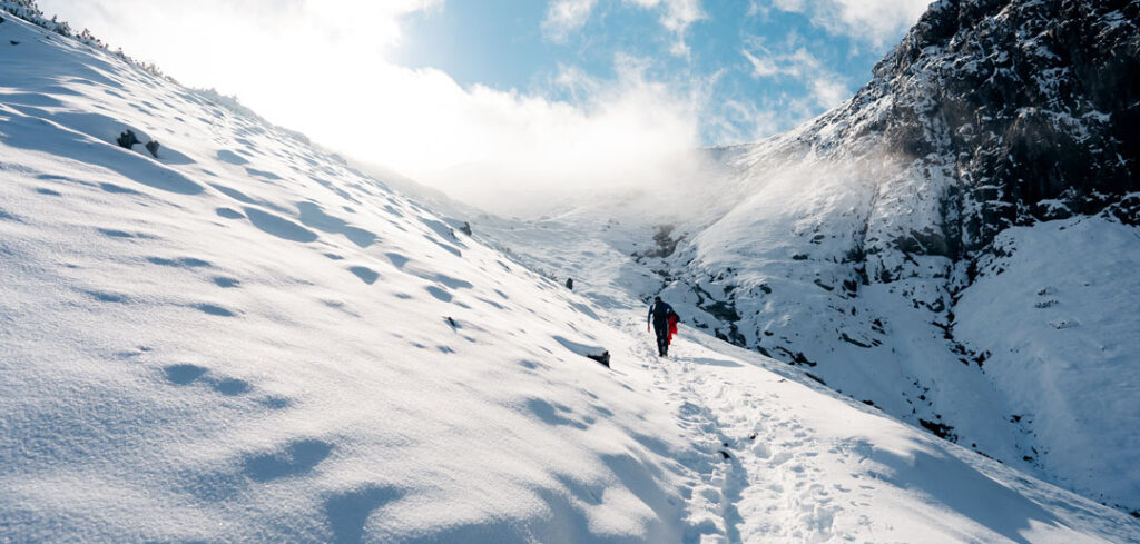 a person hiking up the side of a snowy mountain as clouds roll in