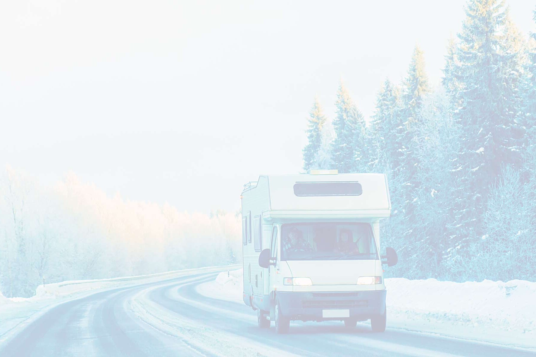 A recreational vehicle driving down a snowy mountain road surrounded by pine trees